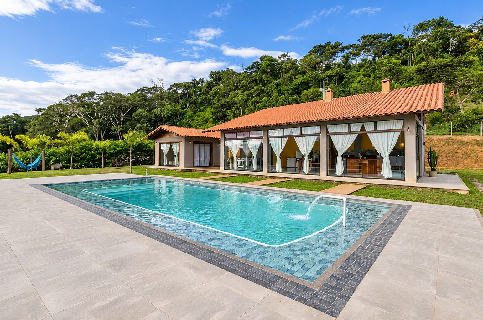 Piscina ampla e a casa de telhado colonial cercada de mata